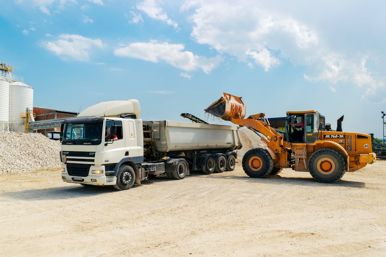 our-services-2 Excavator loading materials into a heavy-duty truck at a sunny construction site.