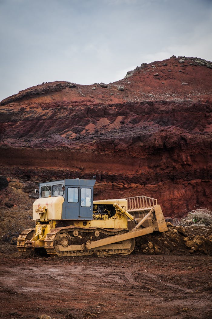 gallery-3 A yellow bulldozer excavating in a rugged red earth quarry under a cloudy sky.