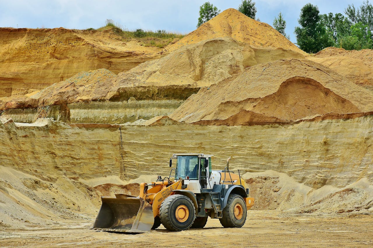 hero-img-01 An excavator working in an open pit mine surrounded by sandy terrain and clear sky.