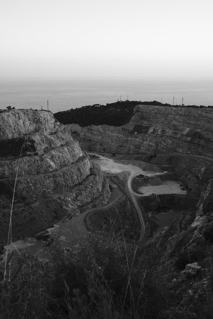 Black and white high angle view of a rugged quarry with roads and hills.